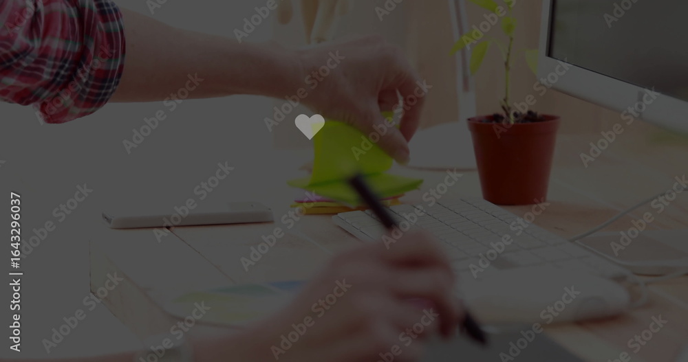 Fototapeta premium Reaching hand in plaid shirt placing sticky notes on office desk, with drawing tablet and stylus