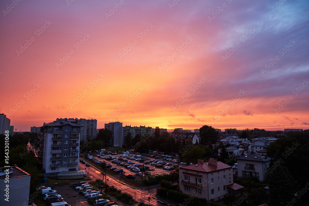 Fototapeta premium Panoramic View of an Urban Area at Sunset with Colorful Sky, Residential Buildings, and Busy Parking Lots