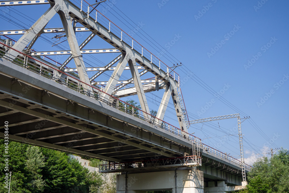 Steel railroad bridge in a mountain valley. Mountain transportation infrastructure. Railroad bridge over green slopes and blue sky Steel railroad bridge in a mountain valley. Mountain transportation infrastructure. Railroad bridge over green slopes and blue sky