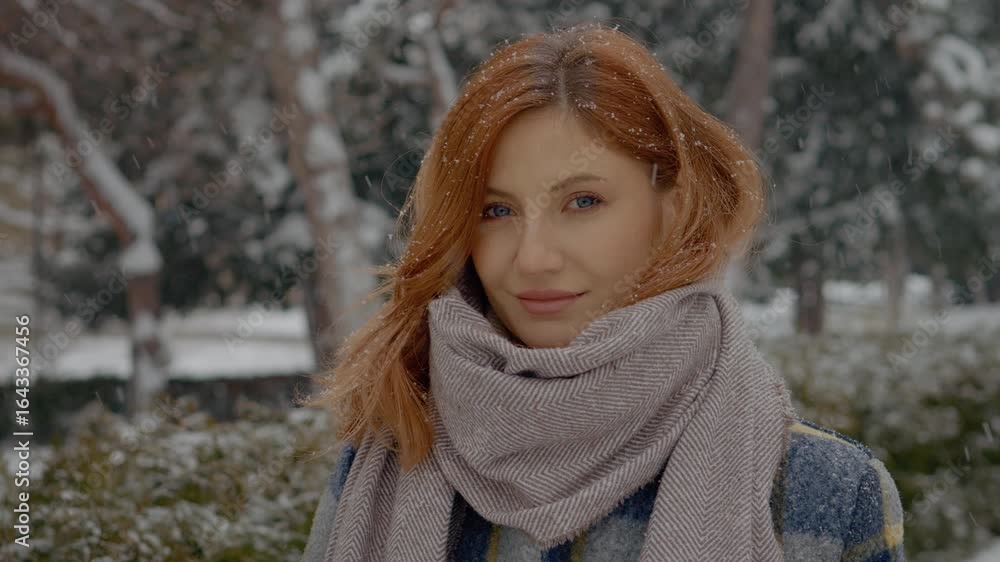 A redhead woman stands in a park during snowfall, wearing a cozy scarf while looking directly at the camera, capturing the serene winter atmosphere around her. A redhead woman stands in a park during snowfall, wearing a cozy scarf while looking directly at the camera, capturing the serene winter atmosphere around her.