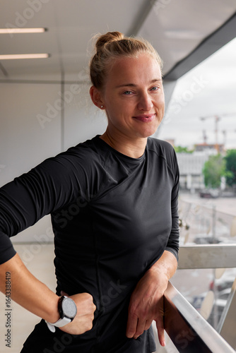 Confident woman in black sportswear leaning on a railing in a bright space Free Download Confident woman in black sportswear leaning on a railing in a bright space - GFXLoad