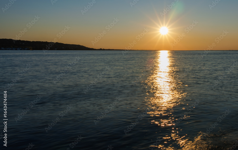 Fototapeta premium Golden sunset over calm ocean waters, with warm reflections stretching to the horizon, serene coastal landscape, tranquil sky, and peaceful seascape perfect for travel and nature themes.