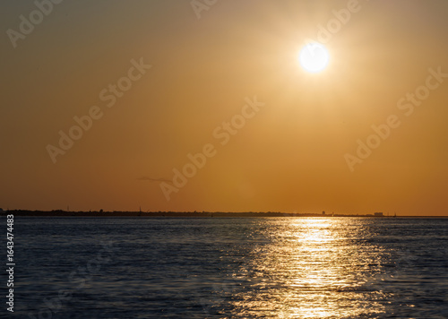 Golden sunset over the ocean with shimmering reflections on gentle waves, an orange sky, and distant horizon, capturing the peaceful beauty of a summer evening by the coast.