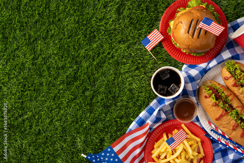 Fototapeta premium Labor Day and Independence Day celebration with American food, including hamburgers, hot dogs, fries, and flags, on a picnic setting representing patriotism