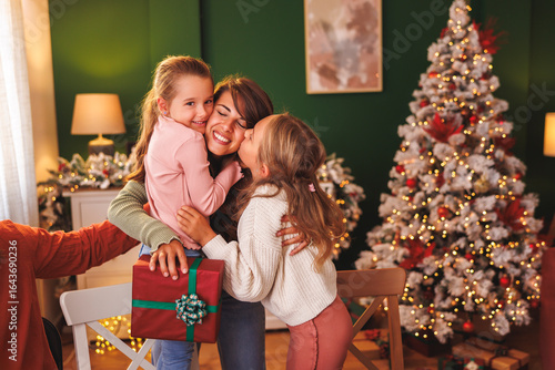 Mother hugging daughters after getting Christmas present over Christmas family dinner at home