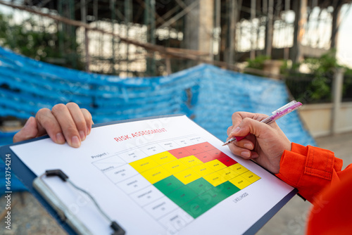 Action of a project manager is writing on risk assessment matrix form to rating the risk of house building structure or building quality (as blurred background. Industrial working scene, close-up.