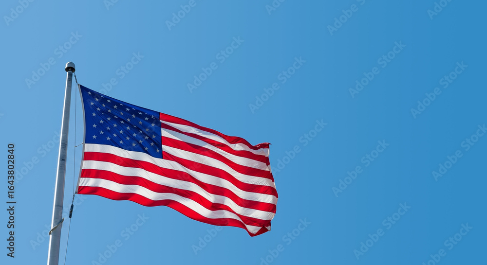 Fototapeta premium The American flag waving proudly in the wind against a clear blue sky