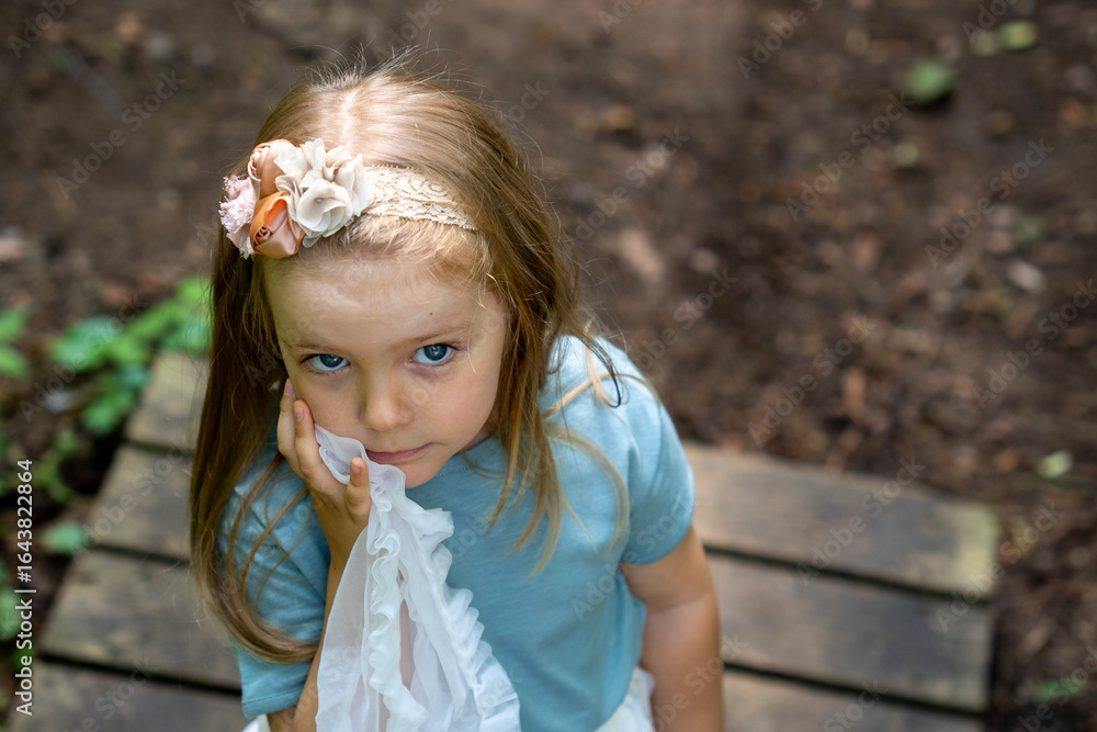 High-angle portrait of a little girl blue t-shirt and white skirt looking up and slightly to the side, standing outdoors in soft natural light with blurred background and copy space for text. High-angle portrait of a little girl blue t-shirt and white skirt looking up and slightly to the side, standing outdoors in soft natural light with blurred background and copy space for text.