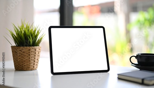 A tablet computer on a white table with a plant and coffee cup.
