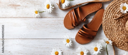 The stylish brown sandals paired with straw hat and flowers on wooden surface