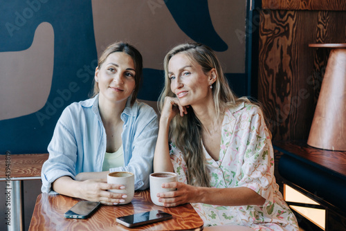 Two middle-aged female friends are gossiping while sitting in a cafe.