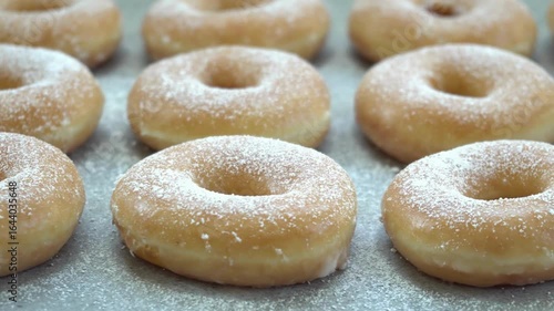 Freshly baked donuts with powdered sugar on a metal tray, close up shot