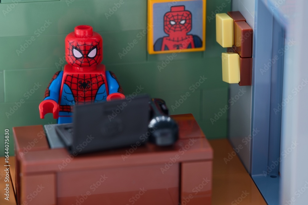 Naklejka premium Tambov, Russian Federation - February 12, 2025 Lego Spider-Man minifigure working behind a black laptop on workplace at the office