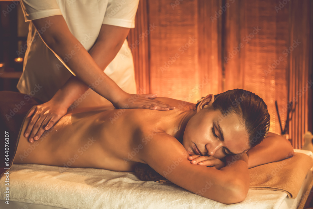 Fototapeta premium Caucasian woman customer enjoying relaxing anti-stress spa massage and pampering with beauty skin recreation leisure in warm candle lighting ambient salon spa at luxury resort or hotel. Quiescent