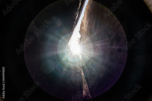 Dramatic sunburst shining through a narrow rock crevice, with visible light rays and lens flare creating a vibrant and dynamic effect.