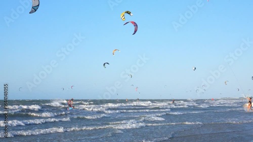 Numerous kitesurfers at Preá Beach, Ceará, Brazil, riding the waves under a blue sky filled with colorful kites.