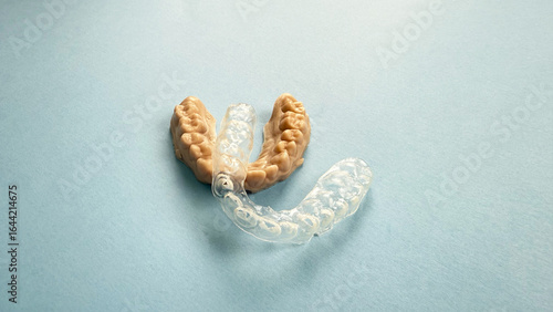 Dental impression of child teeth with transparent worn paediatric mouthguard on blue background, visible scratches and usage marks, female hand holding orthodontic plastic guard for bruxism protection