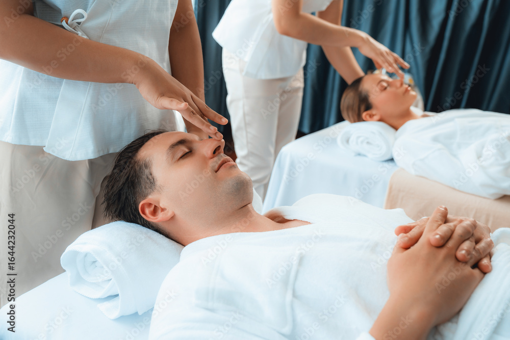 Obraz premium Caucasian couple enjoying relaxing anti-stress head massage and pampering facial beauty skin recreation leisure in dayspa modern light ambient at luxury resort or hotel spa salon. Quiescent