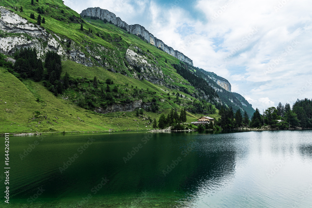 Fototapeta premium Tranquil Seealpsee lake reflecting lush green meadows and towering alpine peaks in the Swiss Alps, creating a breathtaking summer mountain landscape.