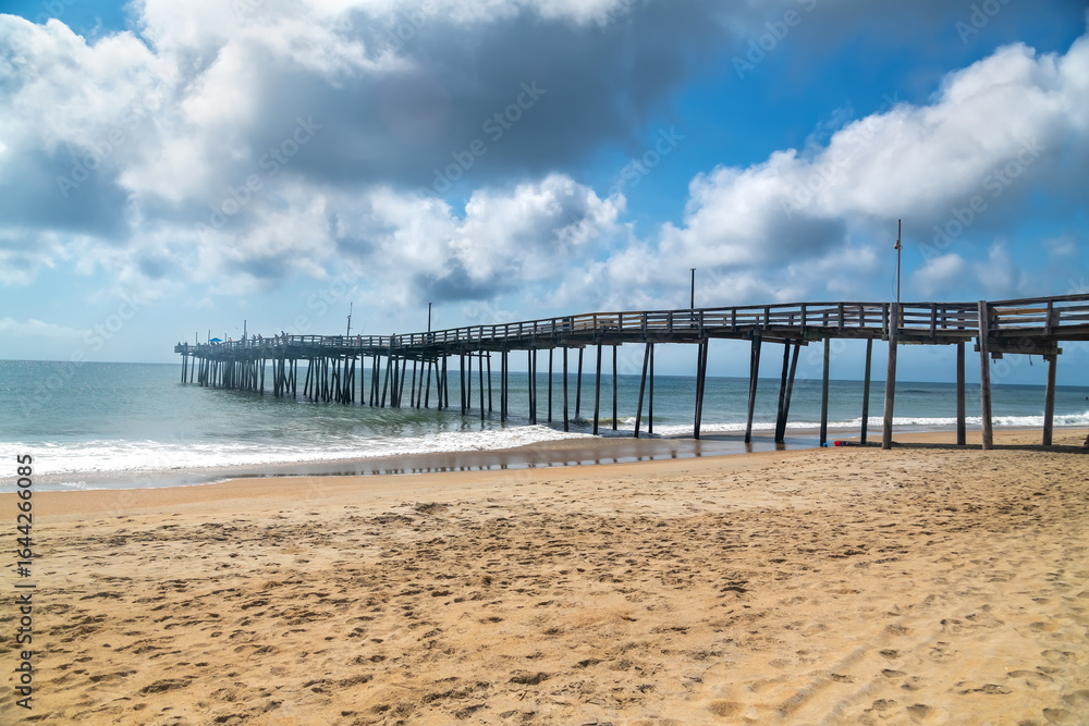 Obraz premium Wooden Pier over Atlantic Ocean. Scenic beach view with clouds and surf.