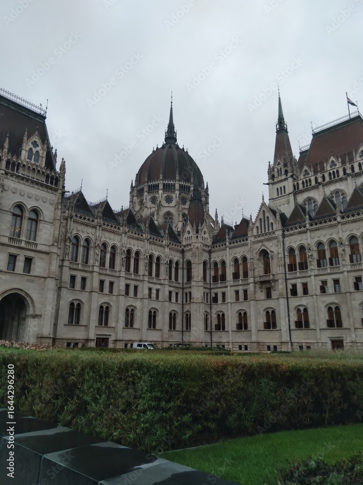 Naklejka premium The front of the Hungarian Parliament Building in Budapest, Hungary, showcases its world-famous neo-Gothic architecture. Decorative spires, pointed arches, and sculpted statues adorn the facade, makin