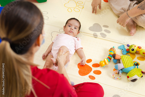 Four-month-old premature baby in motor stimulation therapy with a physical therapist, accompanied by her mother, in clinic, child development