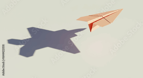 Pink paper airplane with an ambitious shadow of a modern fighter jet.