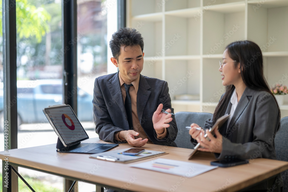 Asian businesspeople discussing work using tablet and documents in office meeting Asian businesspeople discussing work using tablet and documents in office meeting