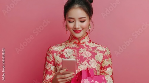 Young Asian woman in traditional dress smiles while looking at her smartphone, holding a gift bag.