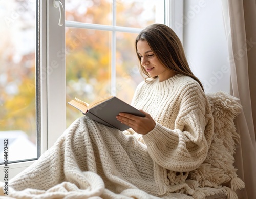 woman reading a book by the window with soft blanket