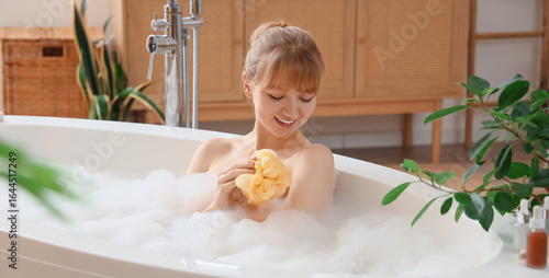Foto Young woman taking bath with loofah and foam at home