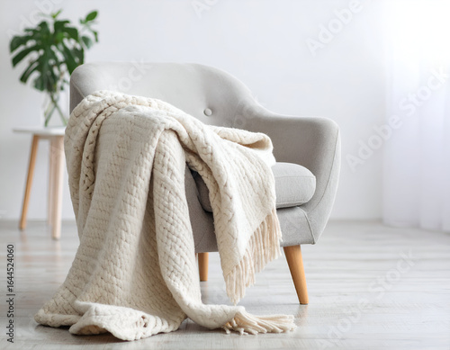 A cozy blank mock up of a soft knitted blanket draped over a modern armchair in a softly lit room, perfect for home decor concepts.