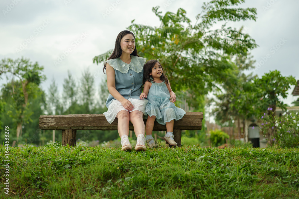 Fototapeta premium happy mother and toddler girl sitting on a wooden bench and talking together in park