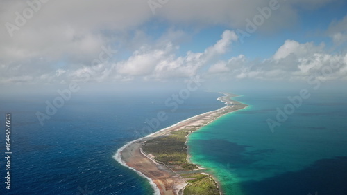 French Polynesia, Rangiroa island: narrow landmass and turquoise water under cloudy sky. Lush greenery borders shoreline, contrast with ocean. Atoll in the Tuamotu Archipelago. Drone flight
