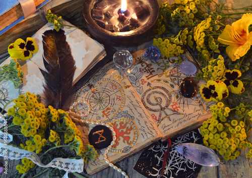 Mystic still life with decorated magic book of spells, tarot card, tansy flowers, crystals, black candles and witchy ritual objects. No foreign language, only fantasy symbols