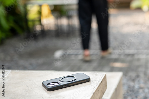 A man in a white shirt is walking past a table with a cell phone on it. The phone is an iPhone