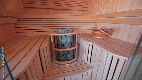 cozy sauna featuring light wood paneling, tiered benches, and a stone heater. A wooden bucket and accessories add to the relaxing atmosphere
