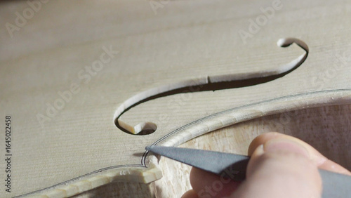 Fotografie Experienced luthier carefully filing delicate f hole curve on violin, revealing