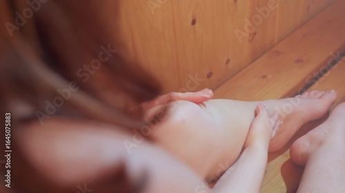 close up of lady with neat polished nails applying cream on smooth leg inside wooden sauna cabin under warm light capturing serene skin care ritual pampering moment
