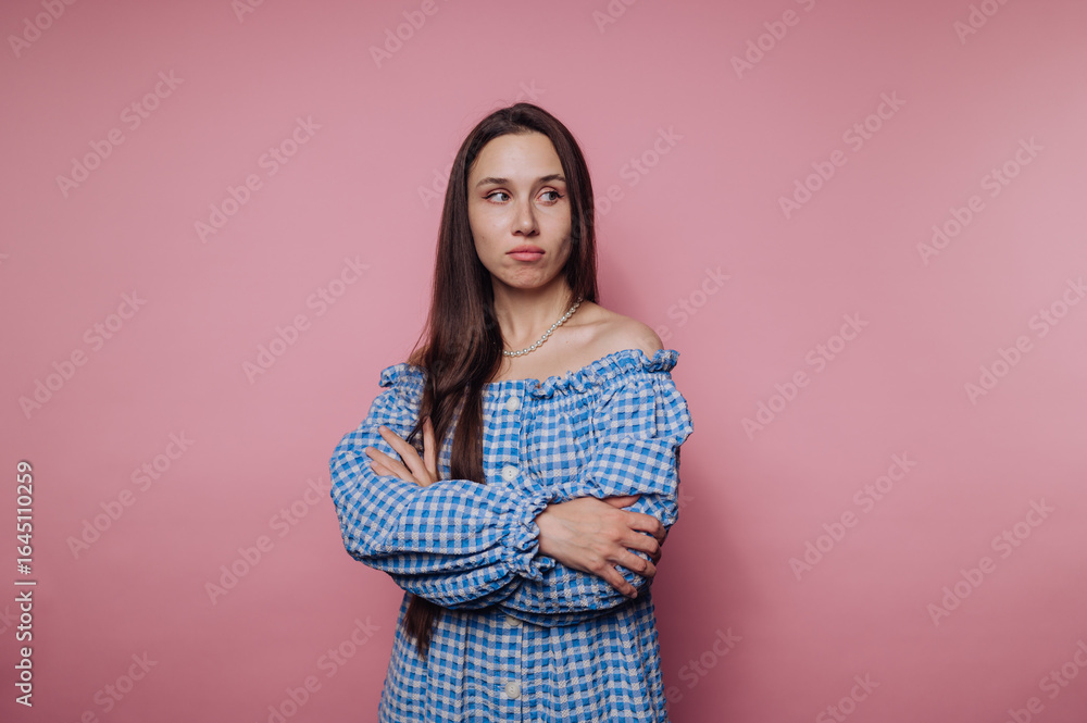 Obraz premium portrait of young thoughtful woman crosses her arms, displaying an expression of contemplation on pink background