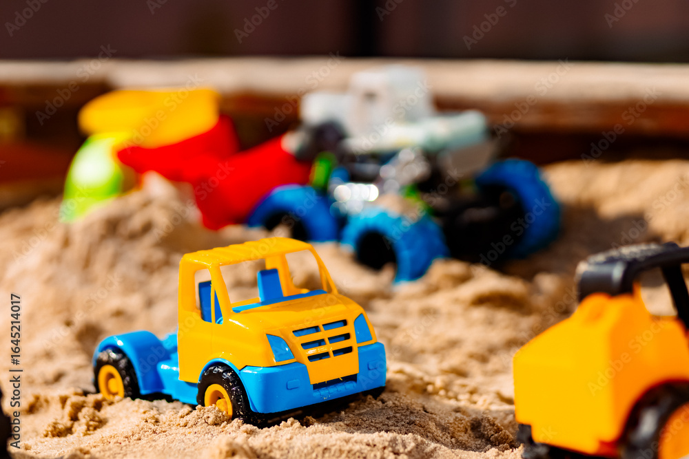 Fototapeta premium Bright toy cars and an excavator standing on the sand. This creates an atmosphere of children's play and creativity.