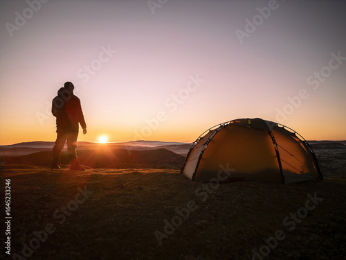 An explorer and his wild camping tent on a hill in England at sunrise