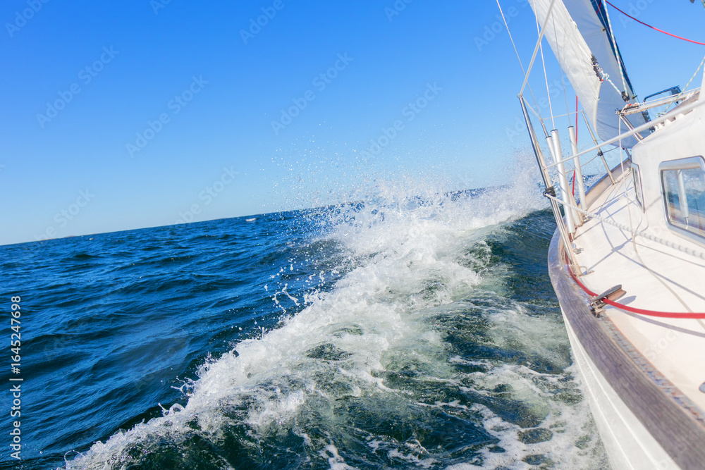 Fototapeta premium Luxury sailing yacht under genoa and mainsail cutting through waves of the Baltic Sea, Gulf of Finland. View from deck to bow, mast, and sails, emphasizing speed, motion, and yachting adventure