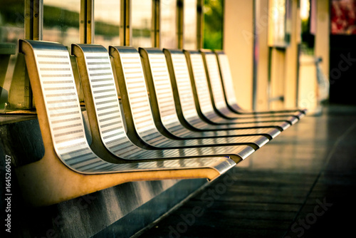 Row of empty metal seats or waiting bench at a train station platform, bathed in warm sunlight