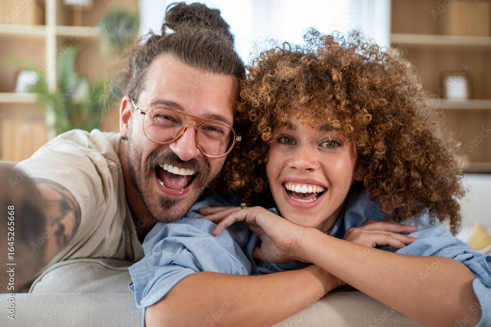 Fototapeta premium Happy couple taking a selfie on the couch, sharing a laugh