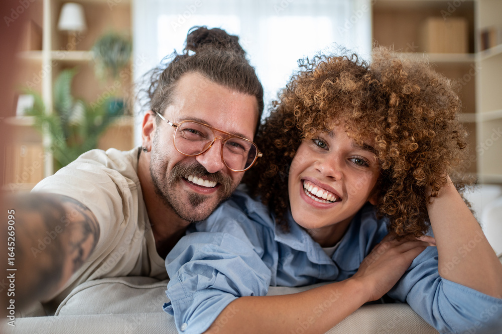 Fototapeta premium Happy couple taking selfie on sofa at home smiling and relaxing