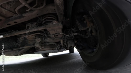 Camera on the underside of a car. The car is driving through the countryside. Focus on the car's suspension