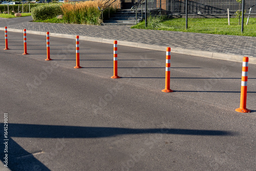 A row of traffic orange striped cones on the road. sunlight. These objects are temporary traffic control devices for directing and avoiding sections of the road being repaired or diverting traffic
