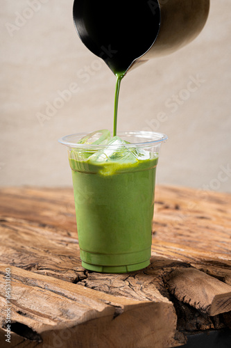Iced matcha latte poured into a clear plastic cup with ice cubes, served on a rustic wooden table for a fresh and vibrant look