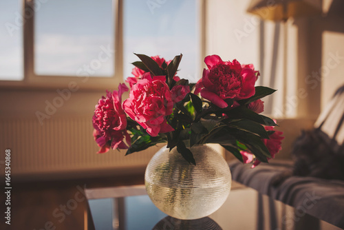 Vibrant peonies bask in golden sunlight on a stylish table, creating an atmosphere of warmth and serenity in a modern living space